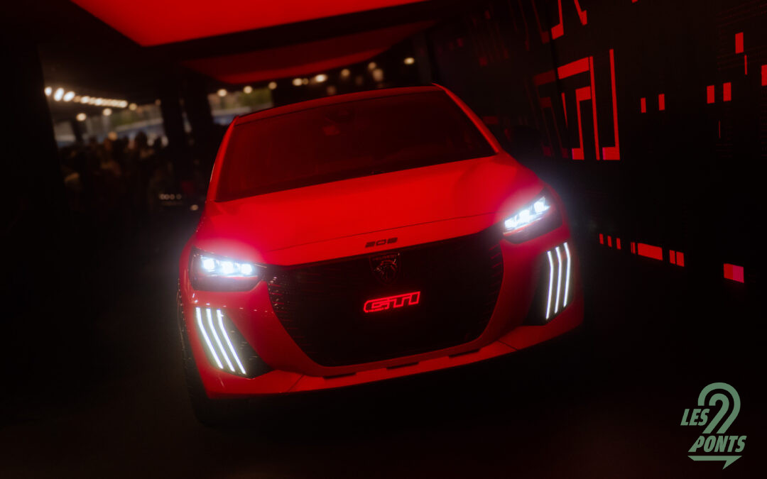 Photo de la e-208 GTi en peinture rouge, vue de face, sur un stand obscurci