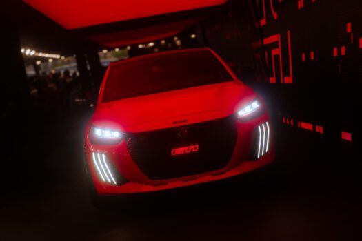 Photo de la e-208 GTi en peinture rouge, vue de face, sur un stand obscurci
